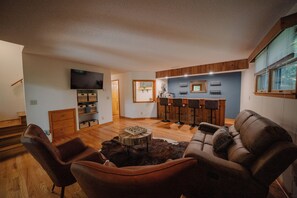 A living room with a brown leather sofa, a coffee table, and a TV mounted on the wall. - Forested 3 BR Cabin with private River/Lake Access Boone/West Jefferson (Fleetwood)