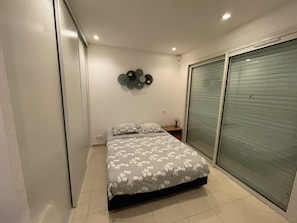 A bedroom with a bed, a wall-mounted decoration, and a sliding door. - An exceptional villa with a pool, right by the sea, combining tranquility and elegance. (Sainte-Maxime)