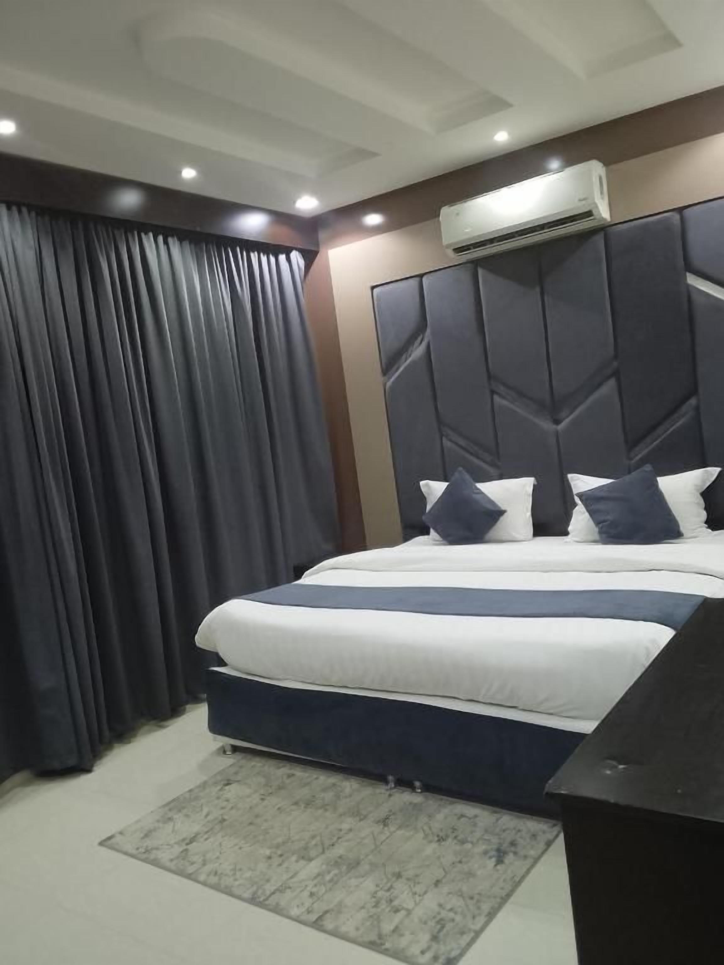 A hotel room with a bed, curtains, an air conditioning unit, and a desk.