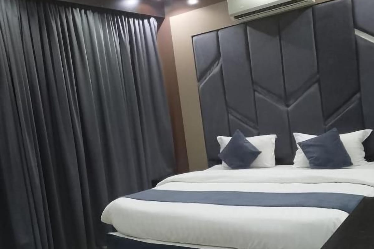 A hotel room with a bed, curtains, an air conditioning unit, and a desk.