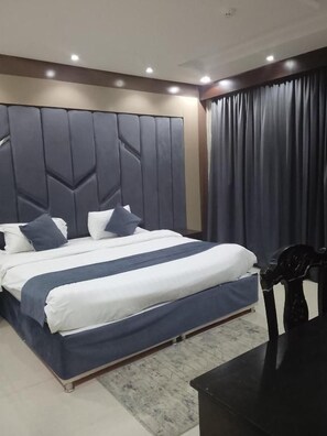 Un dormitorio moderno con una cama grande, cabecera con patrones geométricos, cortina oscura y una mesita de noche.