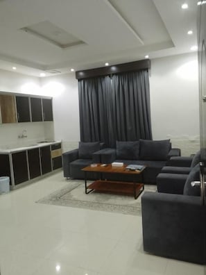 A modern living room with a sofa set, a coffee table, and a kitchen area with cabinets. - aman home 1 for servied apartment  (Al-Khaleej District)