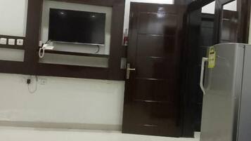 A kitchen with a built-in TV, a refrigerator, and a door leading to another room.
