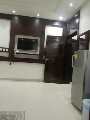 Una cocina con televisión integrada, un refrigerador y una puerta que da a otra habitación.