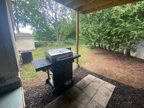 Een buitenbarbecueplaats met een overdekte patio, een houten omheining en een boom op de achtergrond.