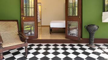 A room with a checkered floor, a bed, a rattan chair, and a decorative urn.