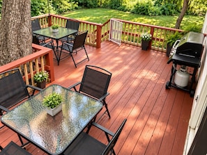 A wooden deck with outdoor furniture, including tables and chairs, and a barbecue grill.