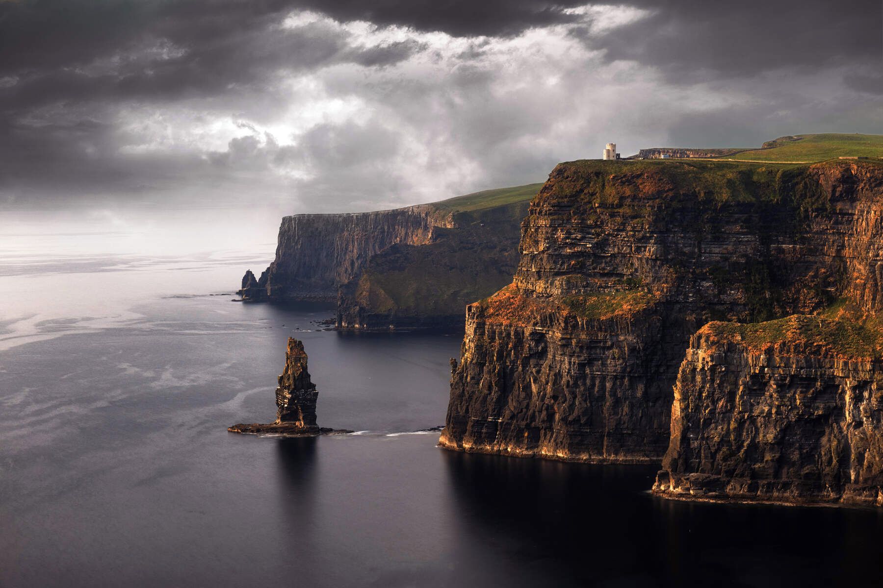 A coastal landscape with cliffs, a lighthouse, and a tower on a hill.