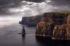 A coastal landscape with cliffs, a lighthouse, and a tower on a hill. - The Galway Getaway-Spacious family room/Perfect to Explore the Wonders of Galway (Galway)