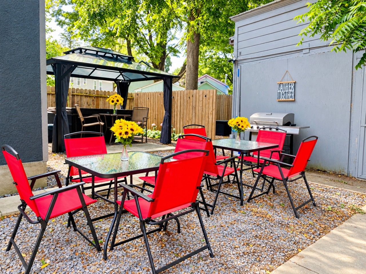 Eine Terrasse im Freien mit roten Stühlen und einem Tisch, einem Grill und einer Pergola mit Sonnenblumen.