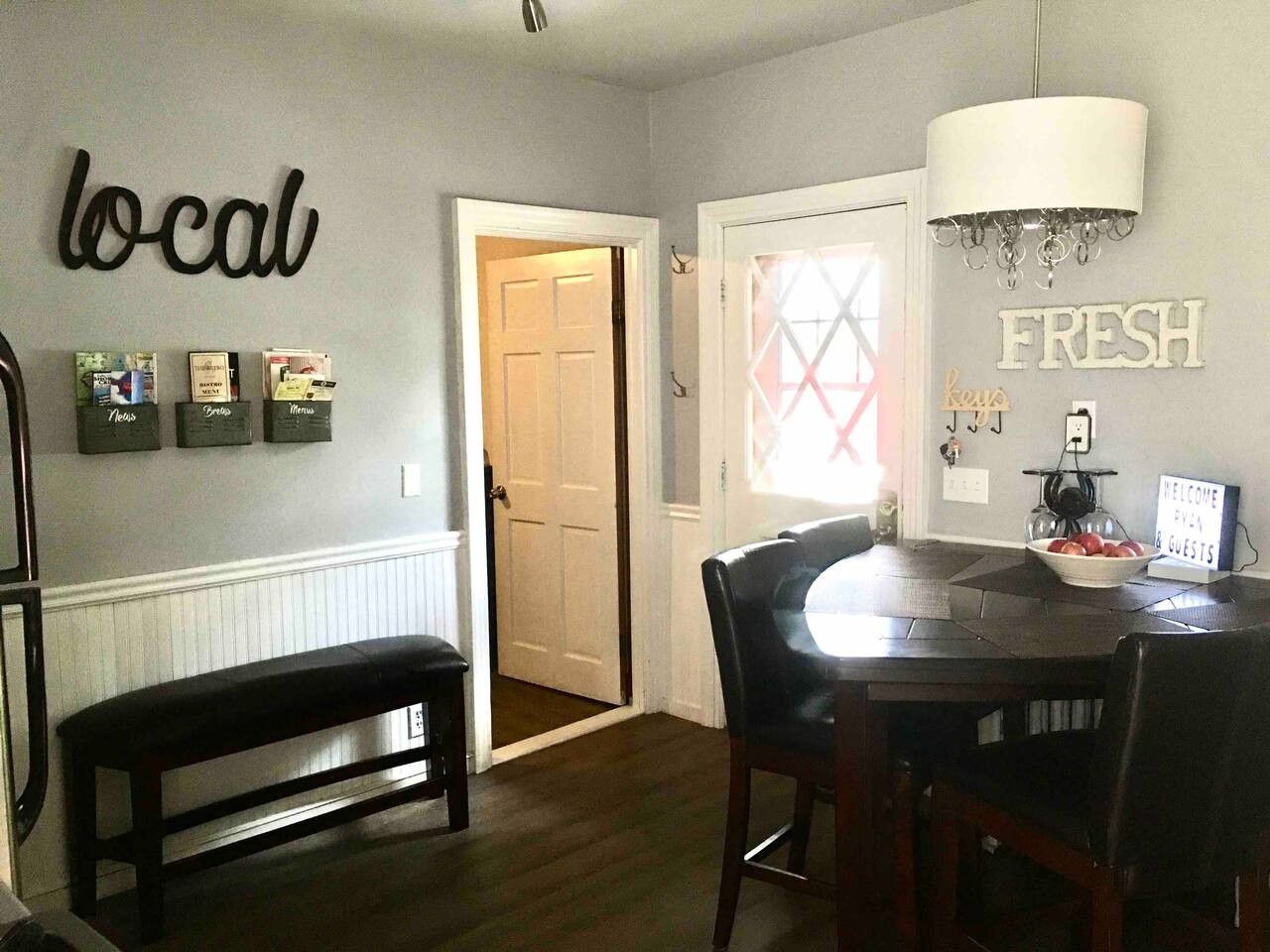 A dining area with a round table, chairs, a bench, and wall decorations including 'local' and 'fresh' signs.