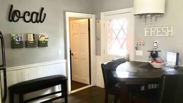 A dining area with a round table, chairs, a bench, and wall decorations including 'local' and 'fresh' signs.