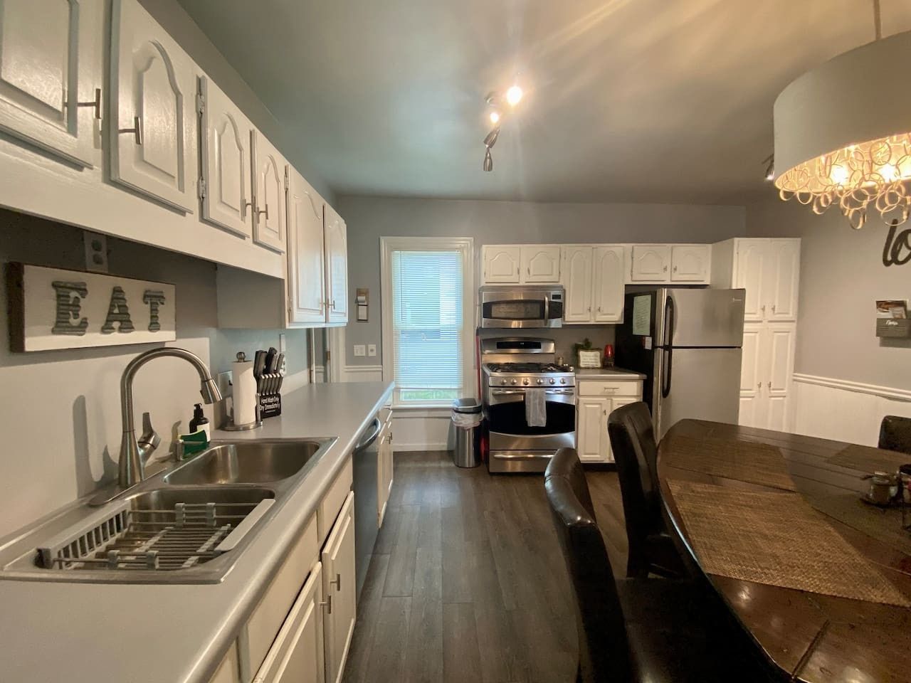 A modern kitchen with stainless steel appliances, white cabinetry, and a dining area with a dark wooden table.