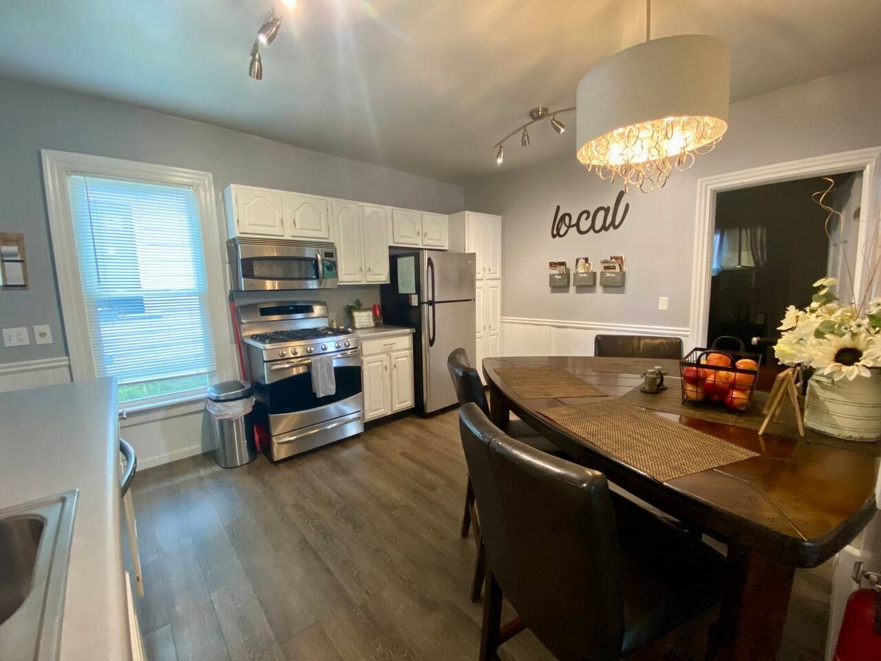 A modern kitchen with white cabinetry, stainless steel appliances, and a dining area with a wooden table and chairs.