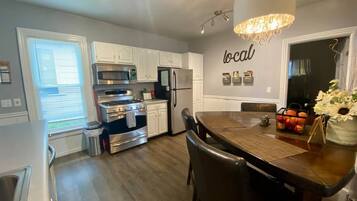 A modern kitchen with white cabinetry, stainless steel appliances, and a dining area with a wooden table and chairs.