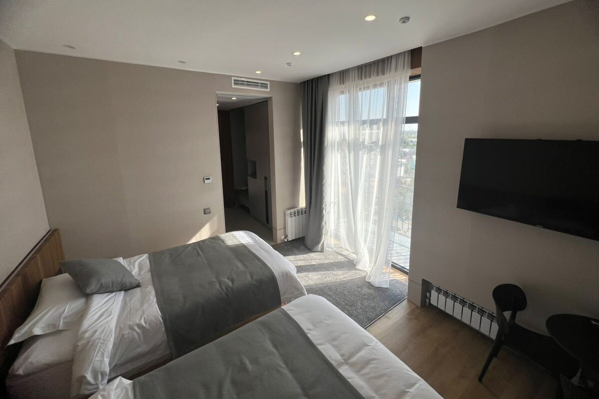 Habitación de hotel con dos camas, televisión y vistas al exterior.