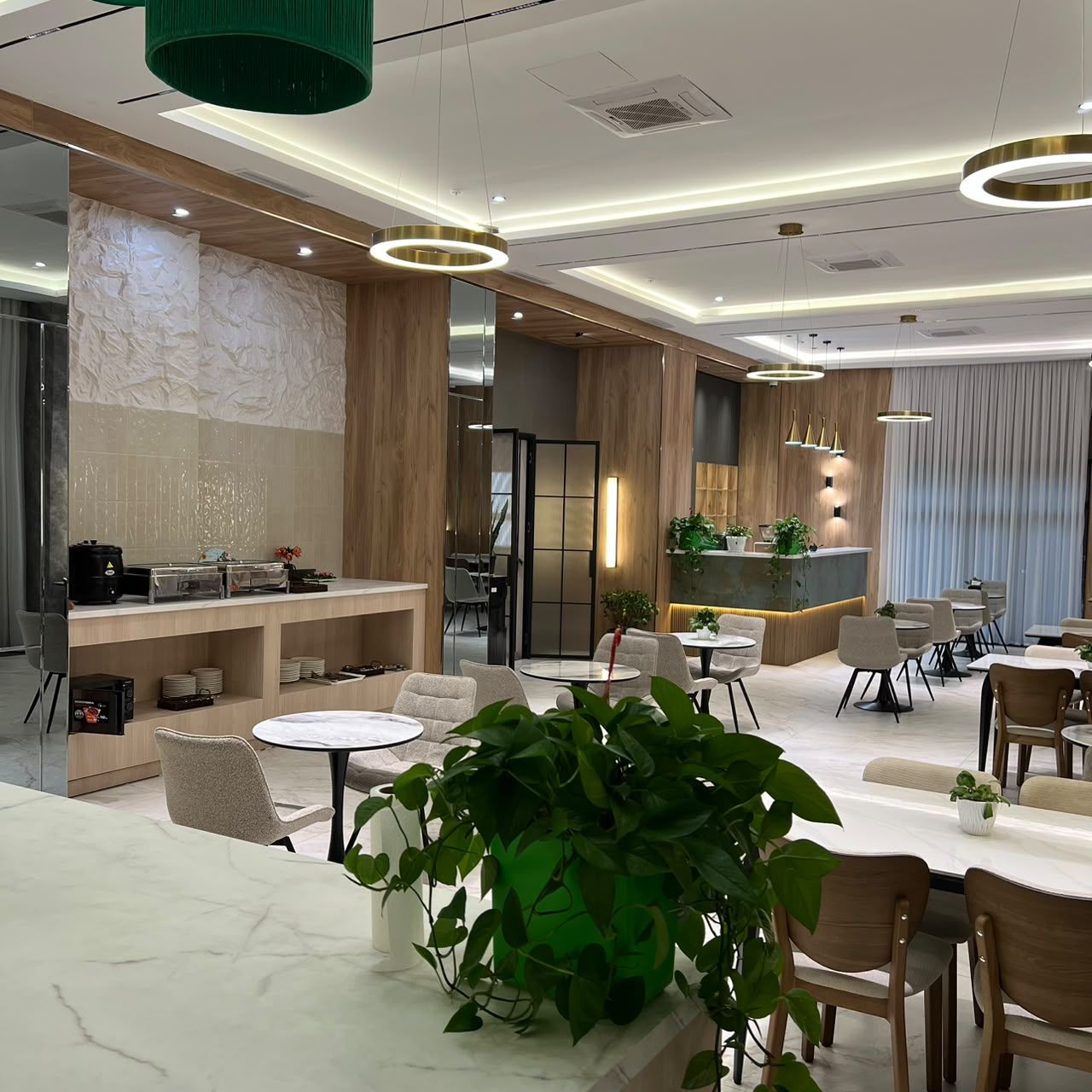 A modern hotel lobby with a reception desk, seating area, and a large green plant.