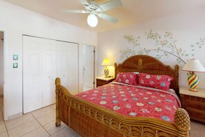 Ein Schlafzimmer mit einem hölzernen Bett, einem Deckenventilator, einem Wandbild und einem Nachttisch mit Lampe.