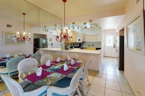A dining area with a glass table, white wicker chairs, and a chandelier. - Family friendly seven mile beach condo.Cayman gem . (George Town)