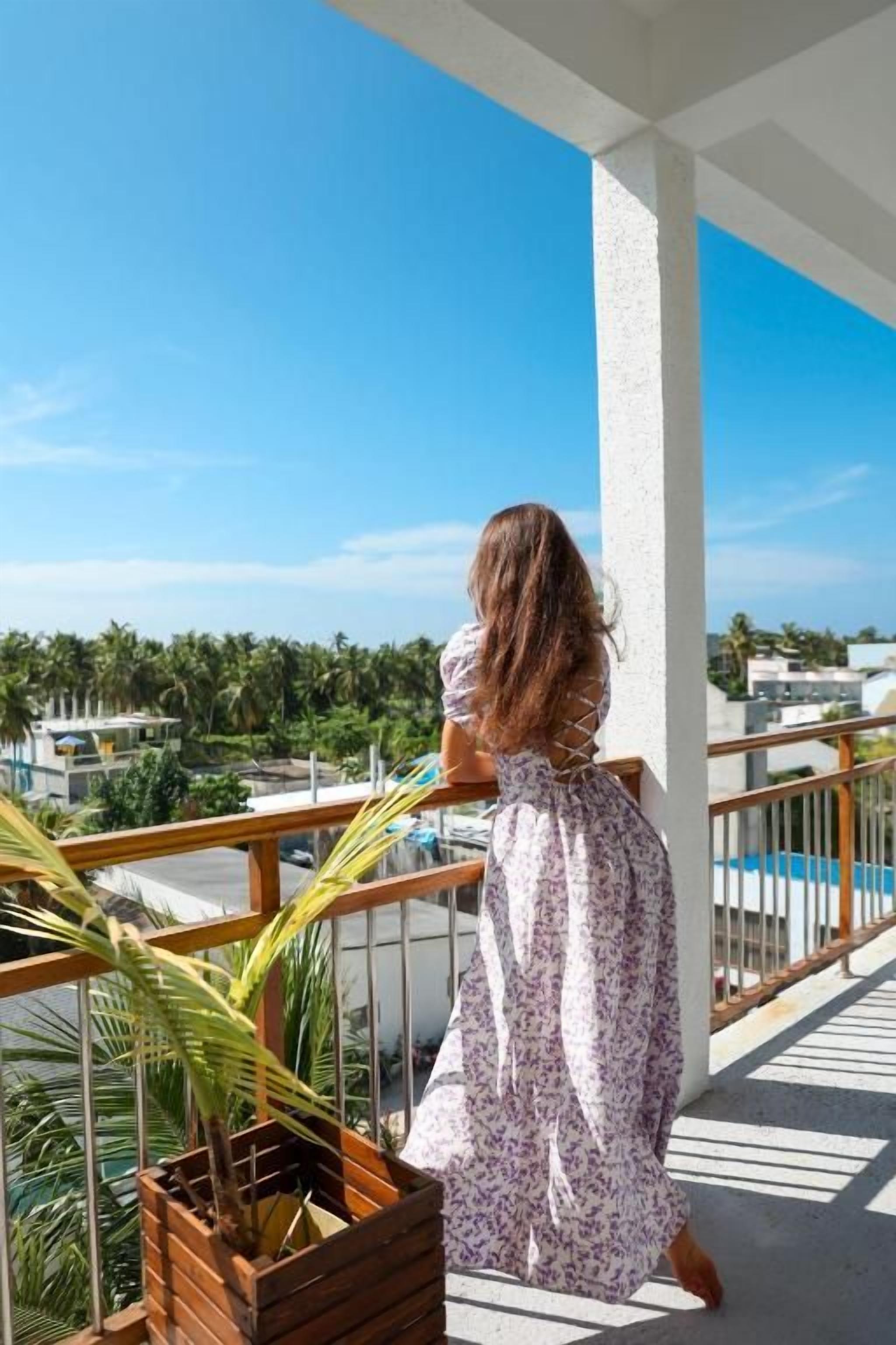 Un balcón con vista a una zona residencial, una jardinera de madera con una planta y una barandilla blanca.