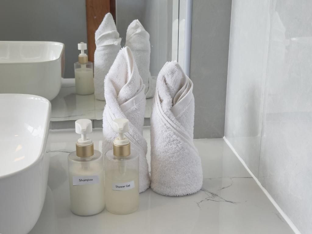 Un baño con un lavamanos blanco, dos botellas de artículos de aseo y una toalla.
