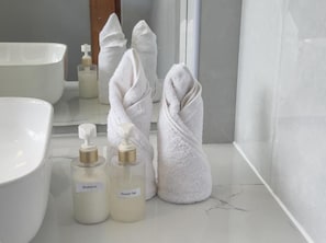 Un baño con un lavamanos blanco, dos botellas de artículos de aseo y una toalla.