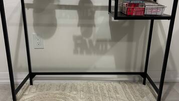 Une pièce avec un bureau à plateau de verre, un vase beige orné de feuillage vert, un tableau encadré et le mot « FAMILLE » écrit sur le mur.