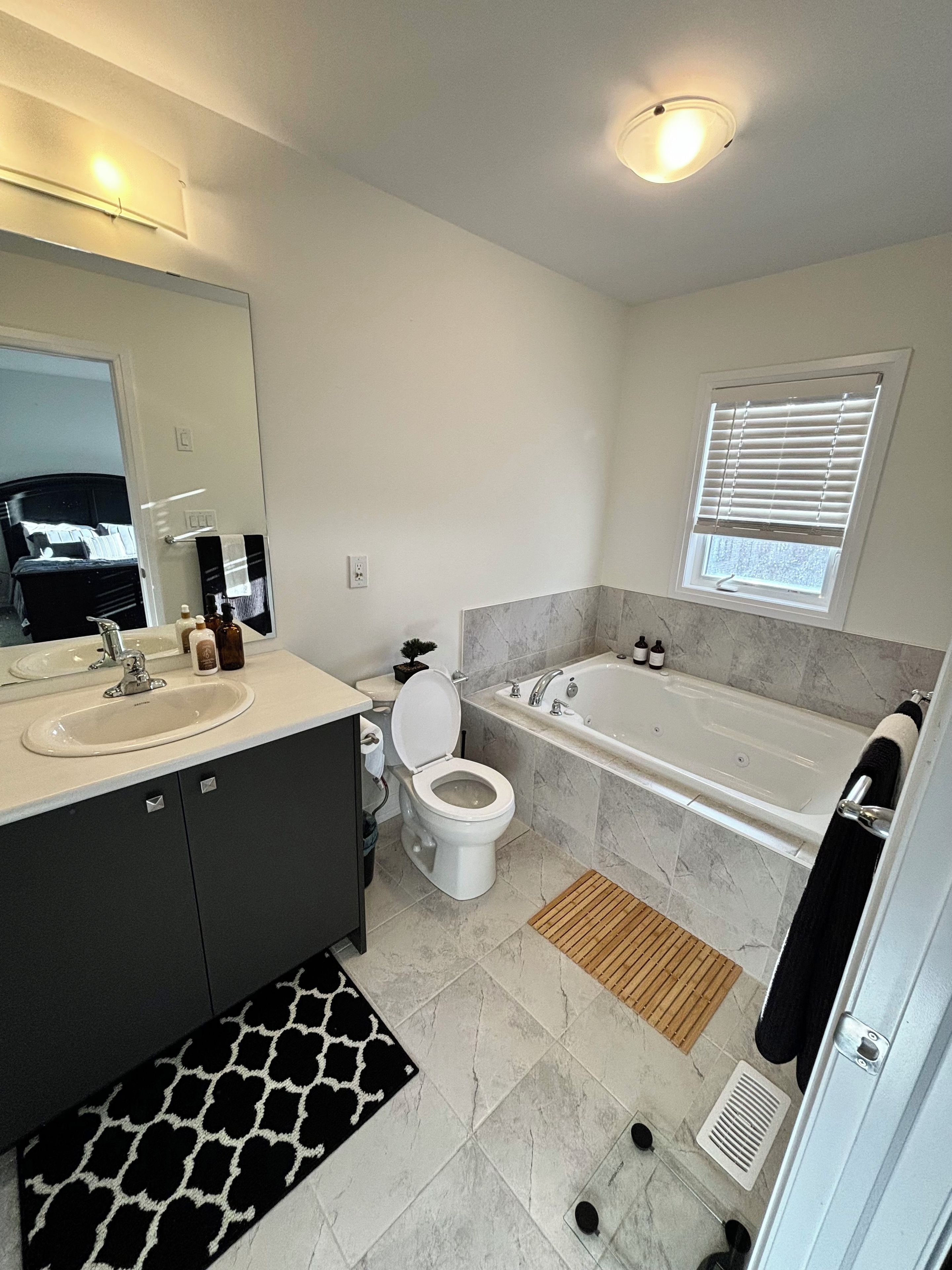 A modern bathroom with a sink, toilet, bathtub, and a window with blinds.