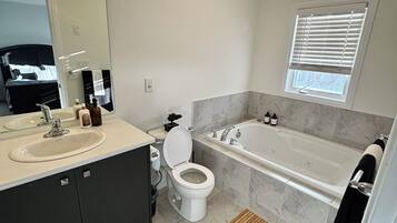A modern bathroom with a sink, toilet, bathtub, and a window with blinds.