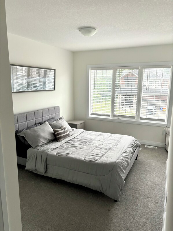 A bedroom with a bed, a headboard, a window with blinds, and a wall-mounted picture.