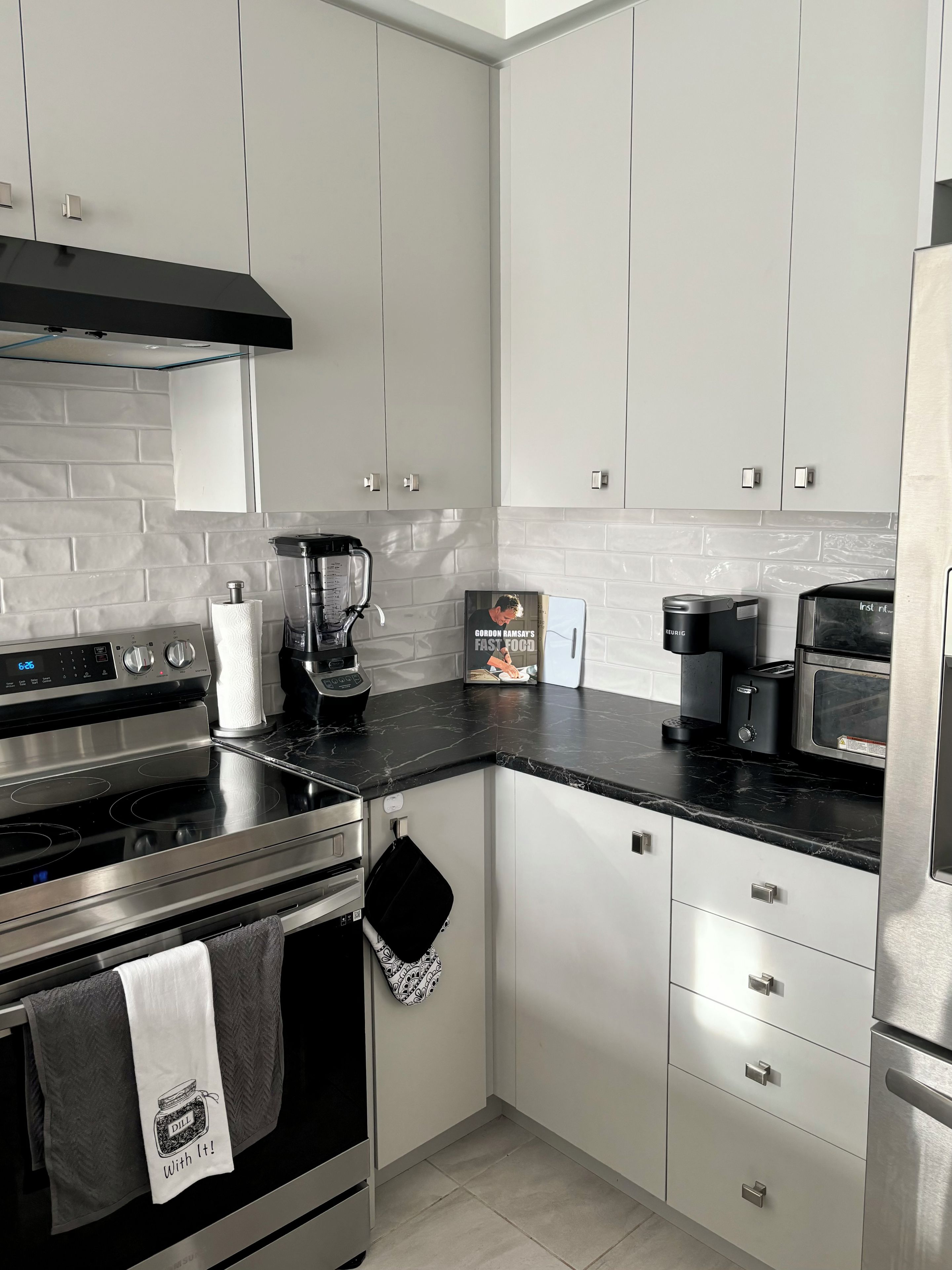 A modern kitchen with white cabinets, a black countertop, stainless steel appliances, and a coffee maker.