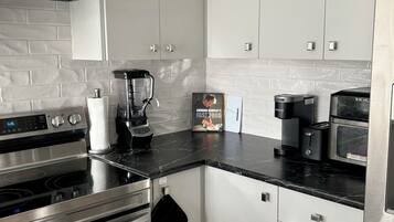 A modern kitchen with white cabinets, a black countertop, stainless steel appliances, and a coffee maker.