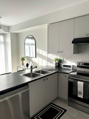 A modern kitchen with a black countertop, stainless steel appliances, and a backsplash.