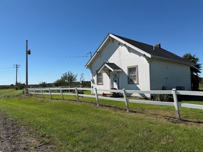 Ein weißes Haus mit weißem Zaun, umgeben von grünem Gras und blauem Himmel.