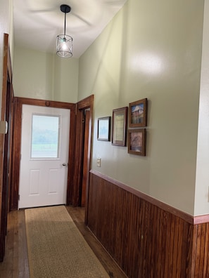 Un couloir avec une porte en bois, un luminaire et des tableaux encadrés accrochés au mur.