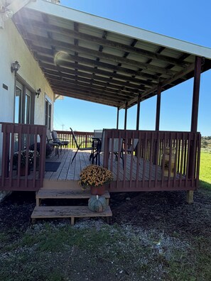 Um terraço coberto ao ar livre com guarda-corpo, mesa, cadeiras e um vaso de flores.