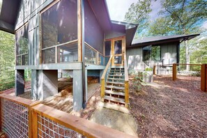 Une maison moderne à deux étages, dotée d’une terrasse en bois et d’un escalier menant à l’étage supérieur.