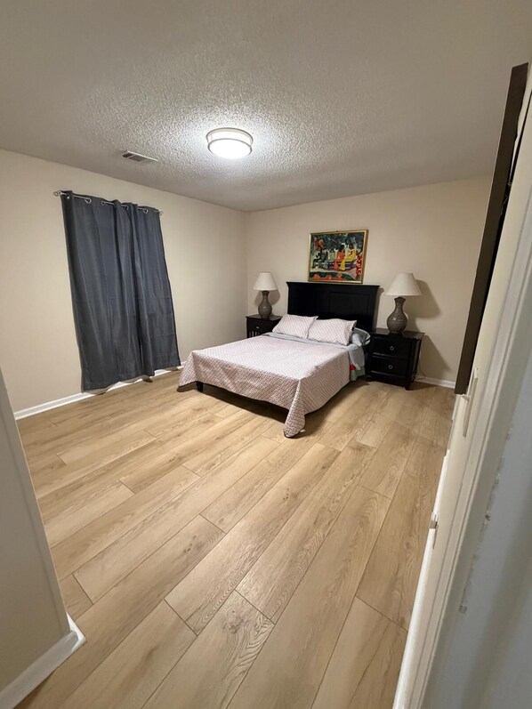 A bedroom with a bed, two bedside tables, a painting on the wall, and a ceiling light. - The Secret Oasis (Lilburn)