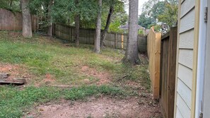 A backyard with a wooden fence, trees, and a grassy area. - The Secret Oasis (Lilburn)