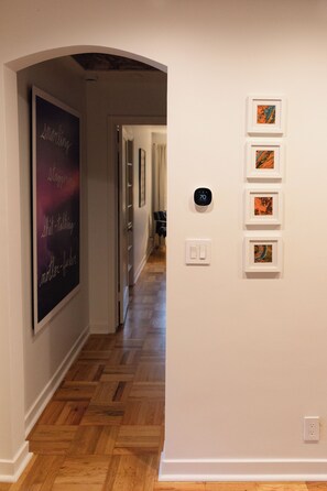 A hallway with a wooden floor, a framed artwork on the left, and a series of framed pictures on the right wall. - Cozy Mountain-View Retreat in Salt Lake City (Salt Lake City)