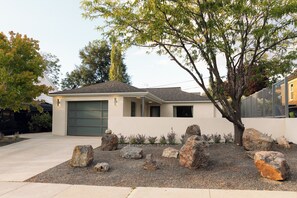 Ein modernes, zweistöckiges Haus mit Garage, umgeben von einem Schotterweg und großen Steinen.