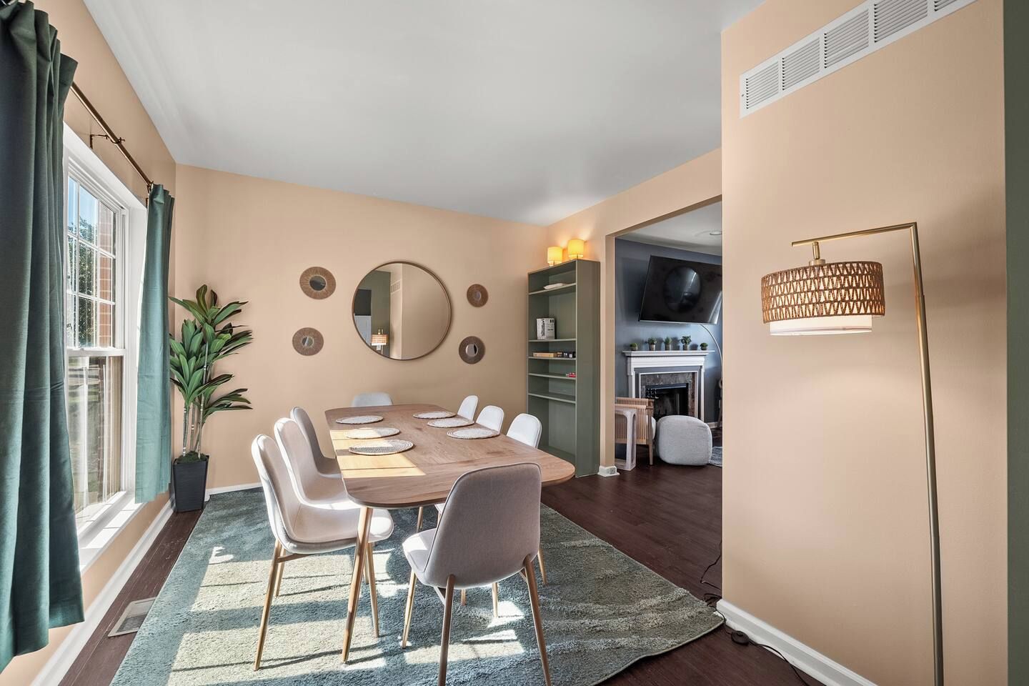 A dining area with a table set for six, surrounded by chairs, a large mirror on the wall, and a bookshelf.