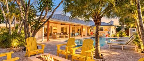 A poolside area with yellow Adirondack chairs, a fire pit, and a pool.