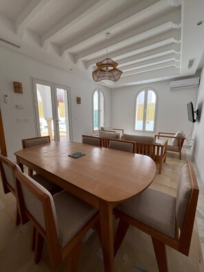 Un comedor amplio con una gran mesa y sillas de madera, una lámpara colgante y ventanas grandes con vistas.