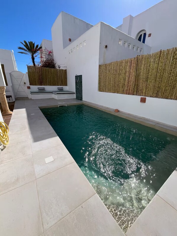 Una piscina con superficie de agua azul cristalina, rodeada de paredes blancas y un suelo con baldosas.