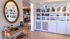 A room with a mirrored wall, a wicker console table with glassware, and a white shelving unit with decorative items. - ccLarge Luxurt\  Home for Groups & Families, Direct on Beach w.Golf Cart (Dorado)