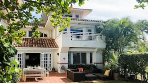 Ein zweistöckiges Haus mit einer Terrasse, Gartenmöbeln und einem Garten.