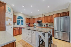 A kitchen with wooden cabinets, a stainless steel refrigerator, and a granite countertop. - The Lobster Cottage - Acadia National Park Retreat (Lamoine)