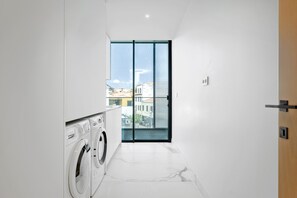 A laundry room with a washing machine and dryer, a glass door leading to a balcony with a city view. - Luxury Three-Suite Residence at Savoy Insular (Funchal)