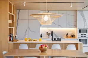 Une cuisine moderne dotée d’un îlot central, d’un dosseret en marbre blanc et d’un luminaire suspendu.